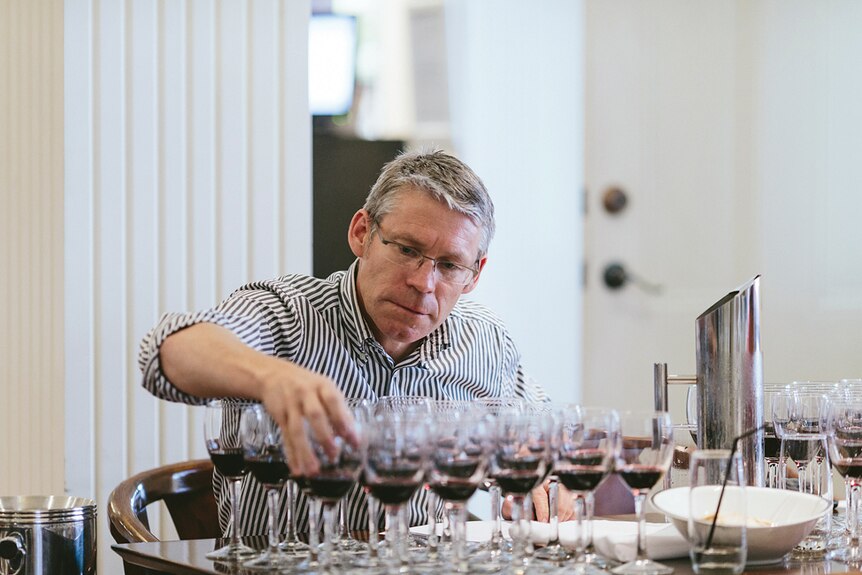 Larry Jorgensen grabs a wine glass from a table full of wine glasses.