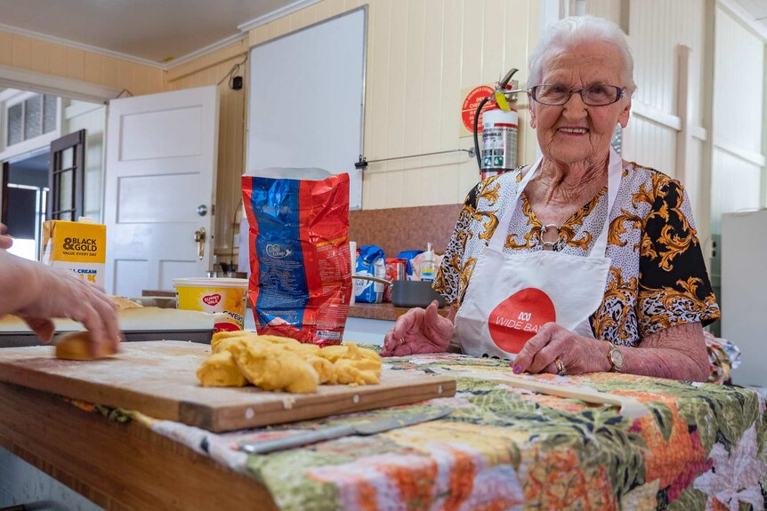 A elderly woman stands in a kitchen making scones.