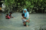 A young man carries an elderly woman across a flooded river.