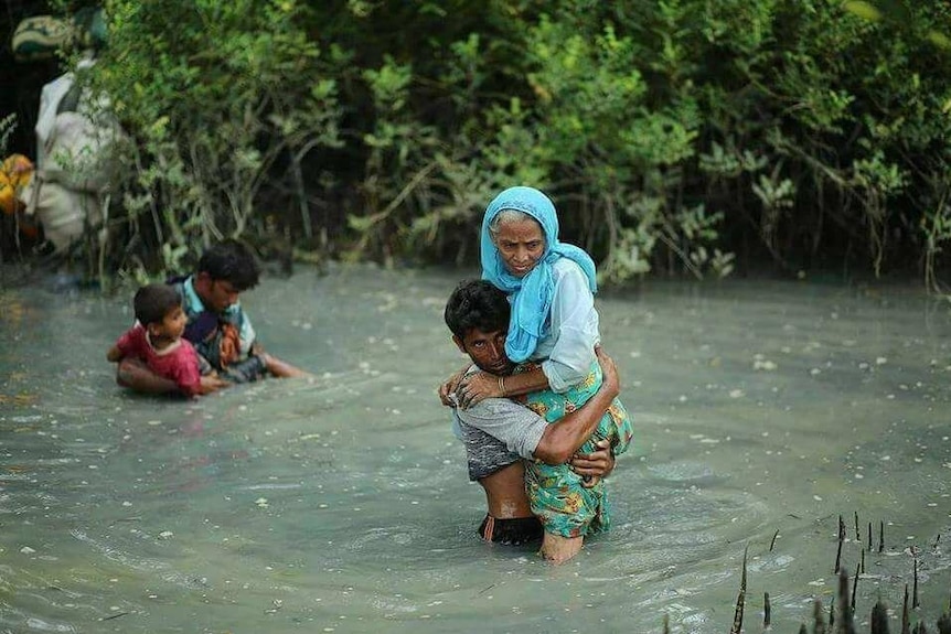 A young man carries an elderly woman across a flooded river.