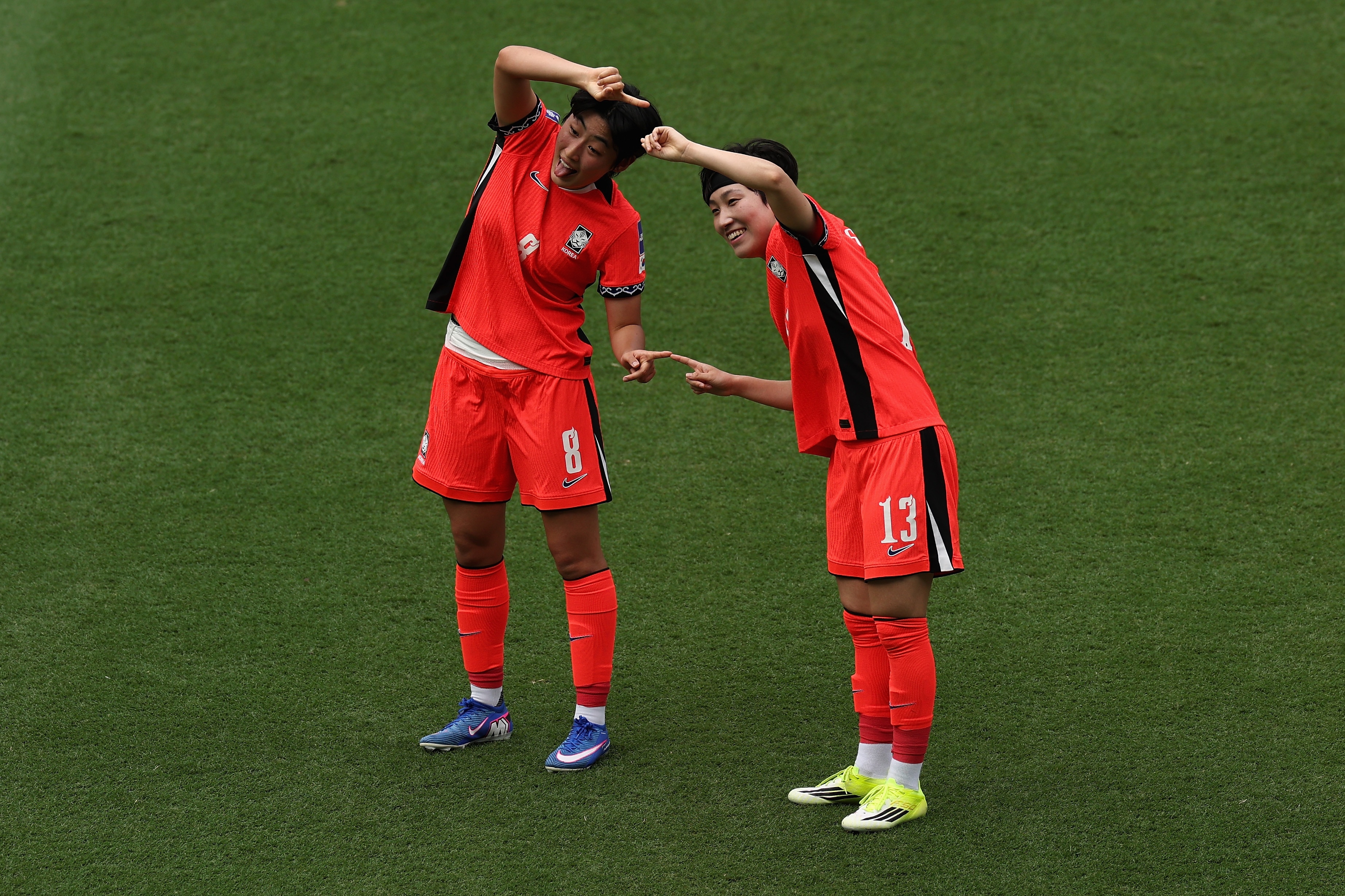 Duas jogadoras da seleção sul-coreana de futebol feminino formam um coração amoroso e sorriem para a câmera