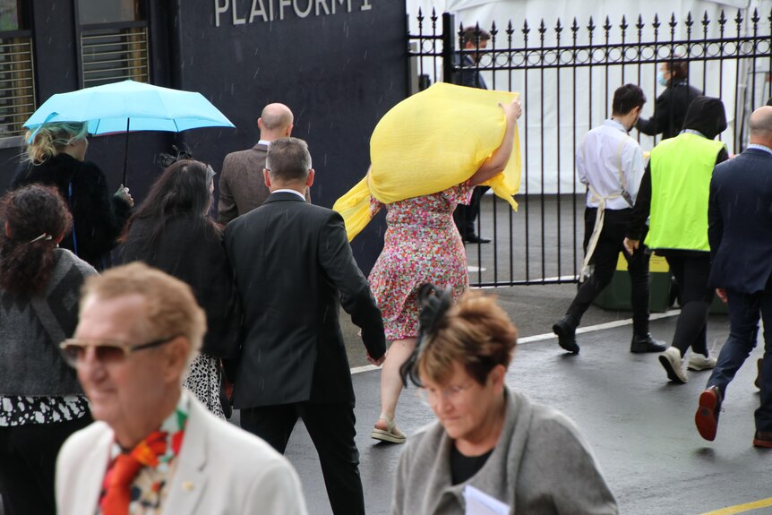 A woman shelters her head with a bag, while another holds an umbrella. 