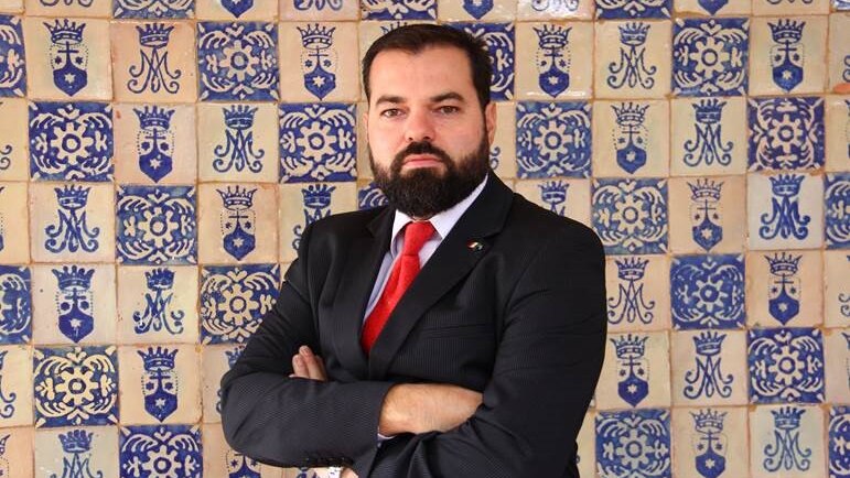 Esau Garza stands with his arms folded against a mosaic background.