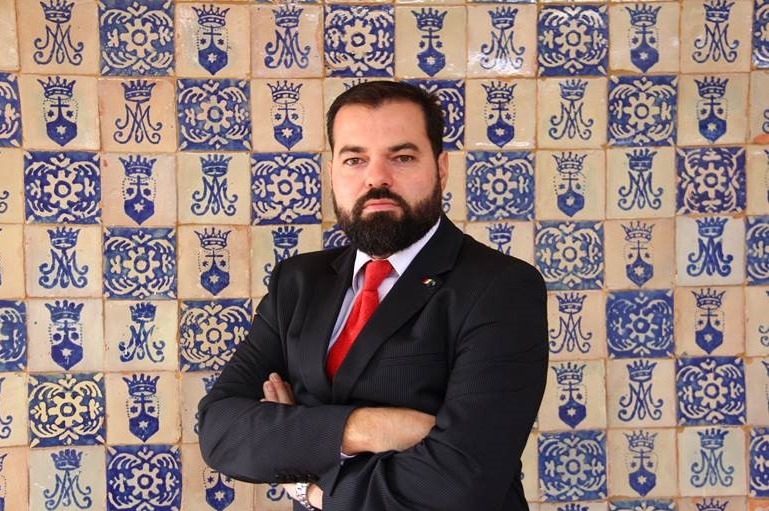 Esau Garza stands with his arms folded against a mosaic background.