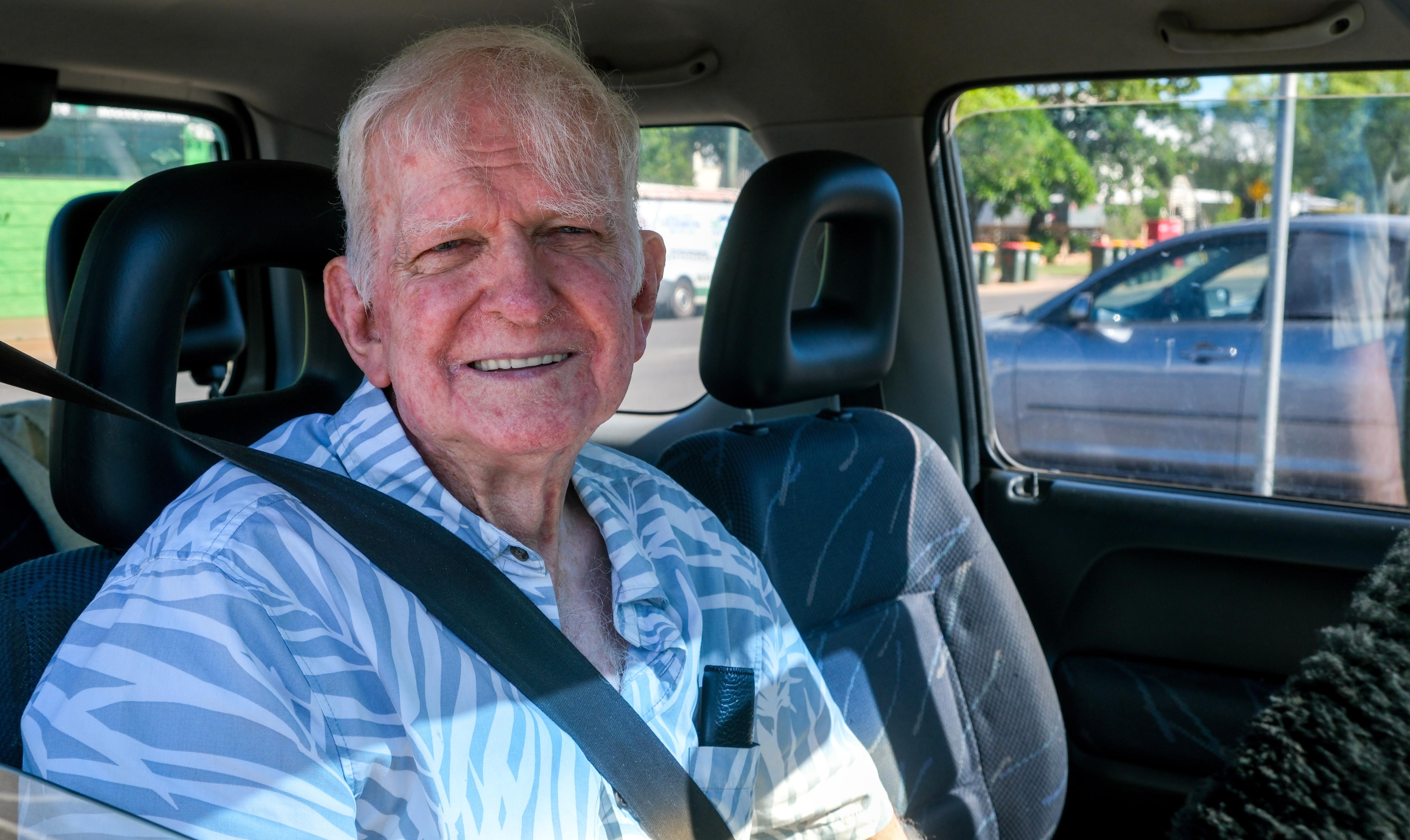 Elderly man in car with seatbelt on smiling.