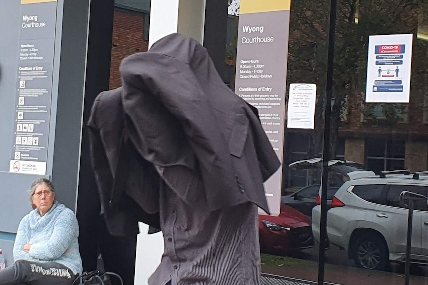 Anthony Lesley Jones with his head obscured by a black jacket runs out of Wyong Local Court.