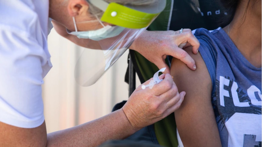A medical worker is giving an injection to someone who rolled up their sleeves.