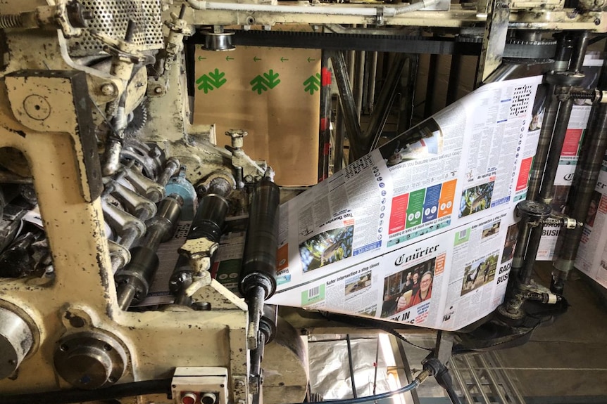 A newspaper is pulled from a printing machine.
