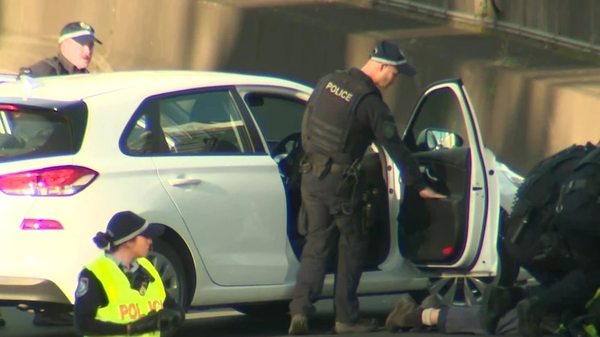 Police standing next to a car and arresting a protestor who blocked the tunnel with a car.