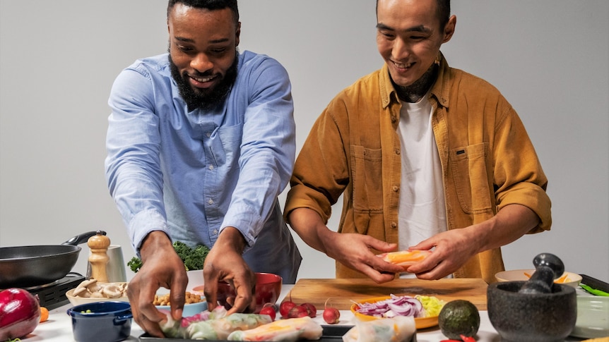 Two men make rice paper rolls.