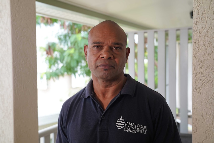 Indigenous man wearing dark navy shirt with the logo for James Cook University Australia.