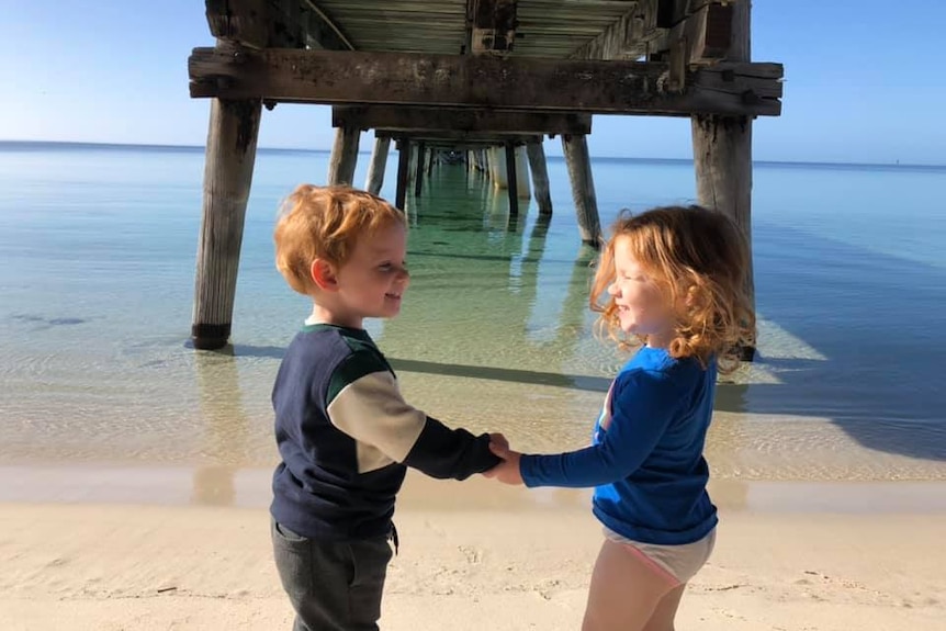 Two cute young toddlers smiling at eachother.