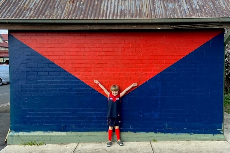 A boy stands against a mural with his arms raised.