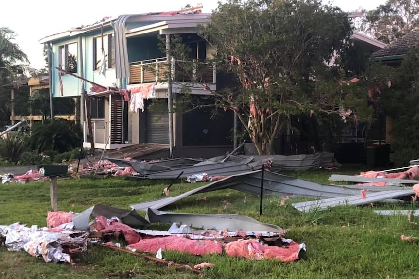 House ripped apart by a storm, installation bats and roofing strewn over front yard.