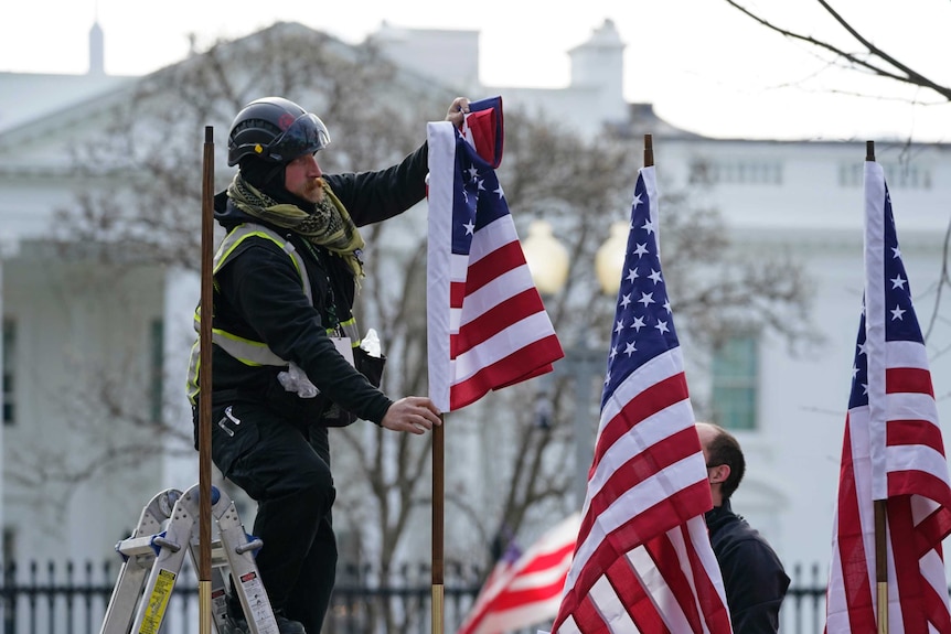 A man up a ladder adjusting American flags outside the White House