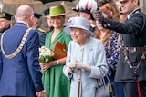 Queen Elizabeth smiles at an official holding a cane and dressed in light blue