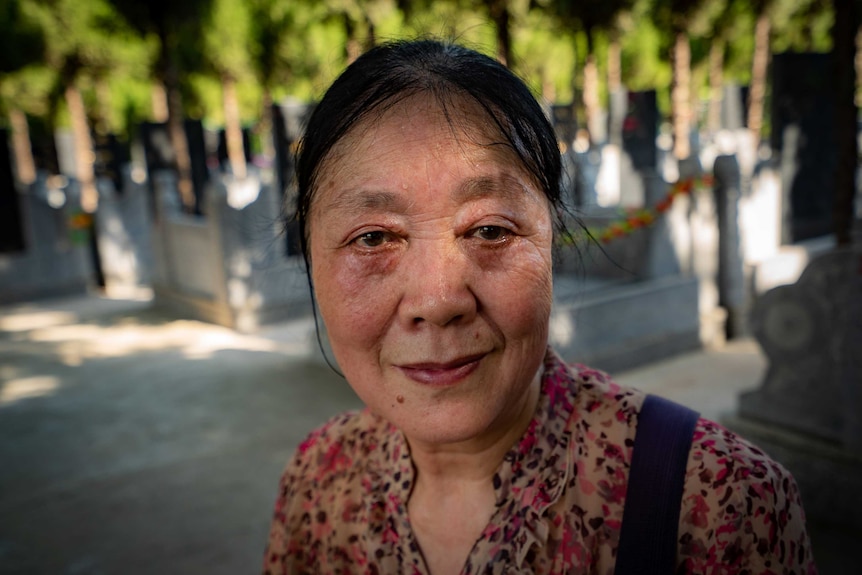 A woman, her face wet with tears, in a cemetery