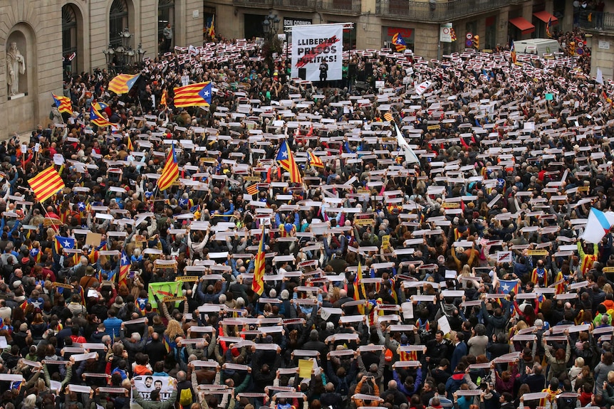 People pack a square in Barcelona, holding up banners.