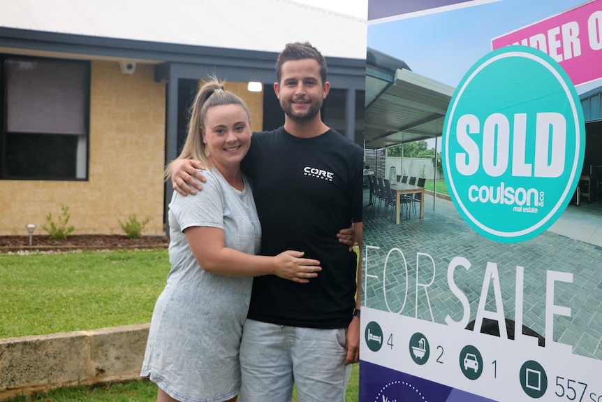 A young couple in front of a real estate for sale sign.