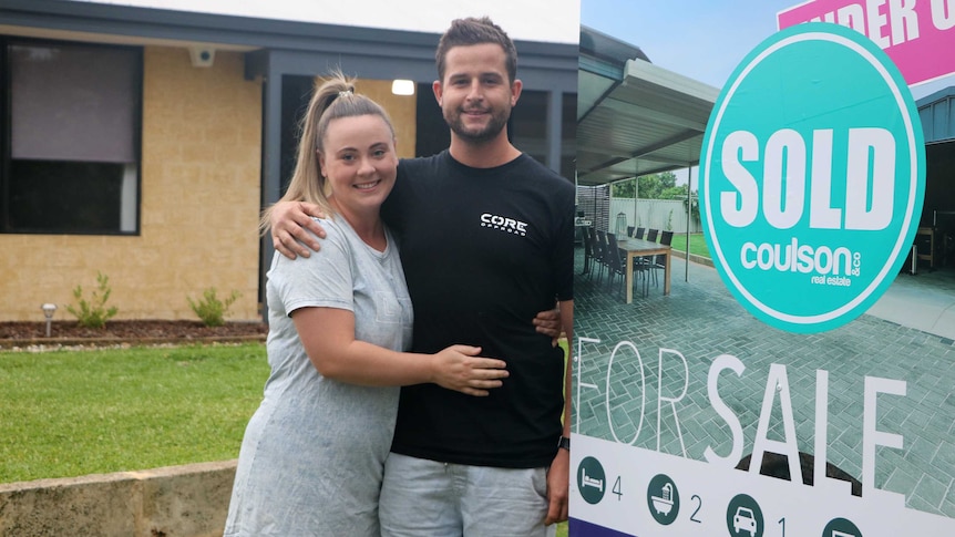 A young couple in front of a real estate for sale sign.