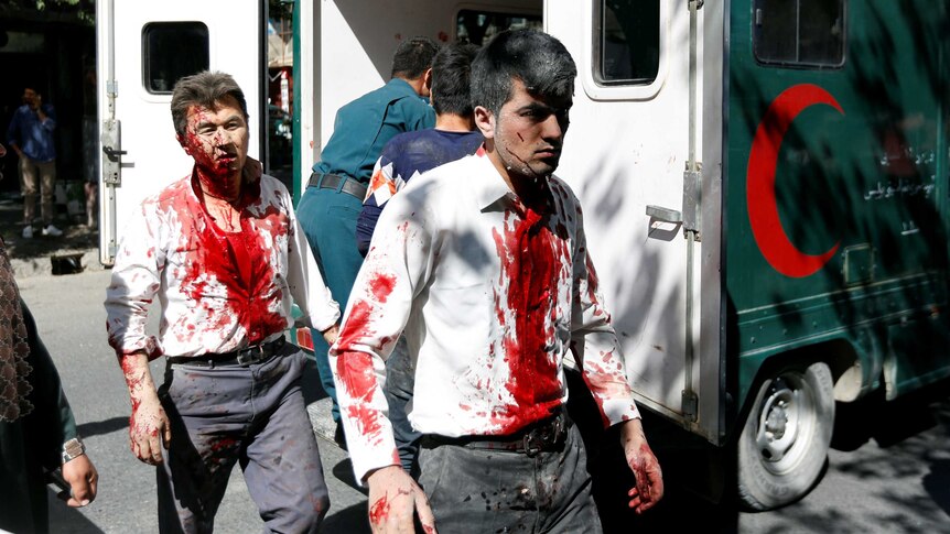 Two men with blood on their faces and down their shirts walk past an ambulance in Kabul.