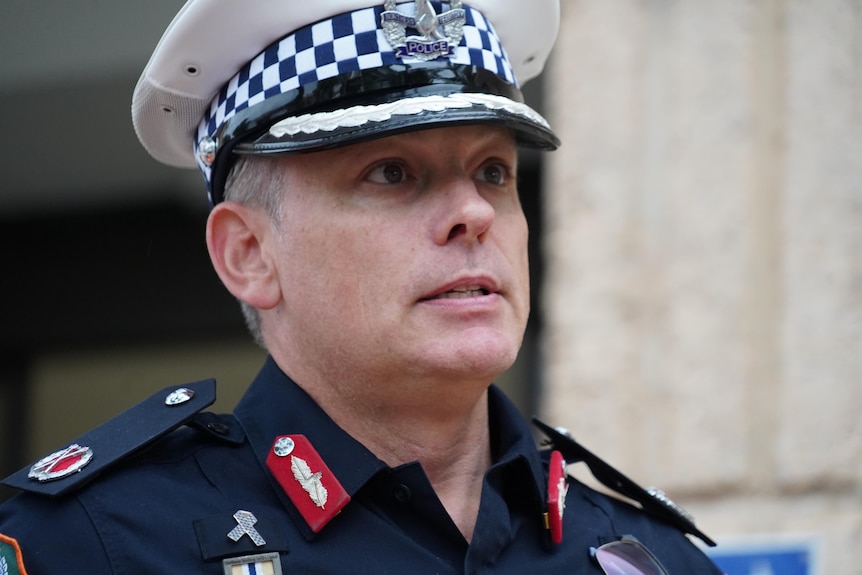 A close up shot of a man wearing a police hat and uniform walking down the front steps of a building