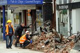 Structural inspectors crouch by rubble and check the condition of a building