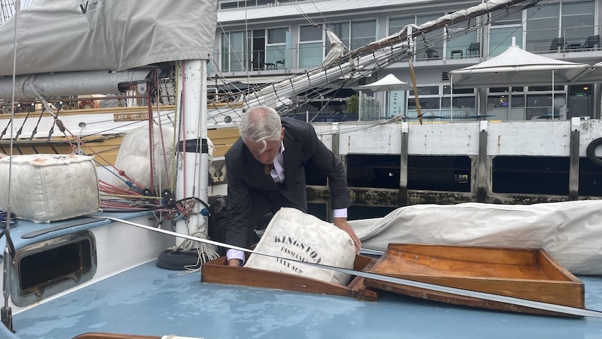 Man in a suit puts a hessian bag of wool into a wooden boat