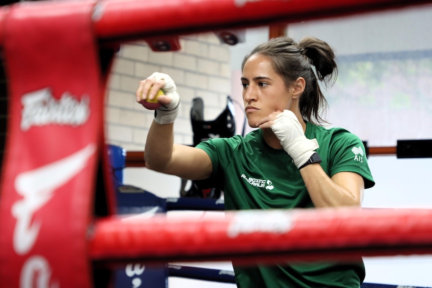 A female boxer is in the ring sparring by herself.