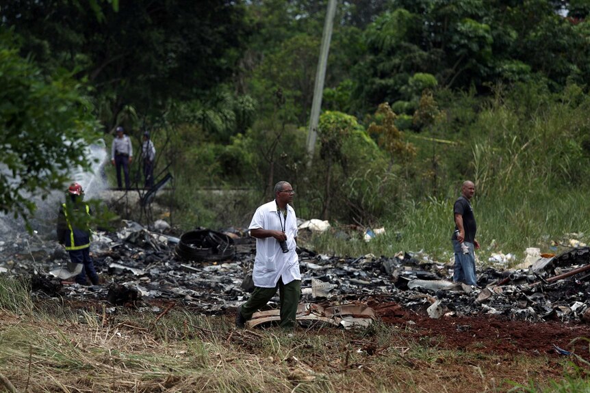 A man with a camera walks past a long, low pile of blackened debris in the field