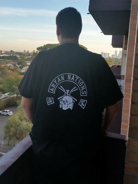 The back of a man wearing a black Aryan Nations t-shirt while standing on a balcony overlooking the Perth skyline.