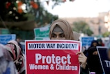 A woman holds a sign reading 'protect women and children'