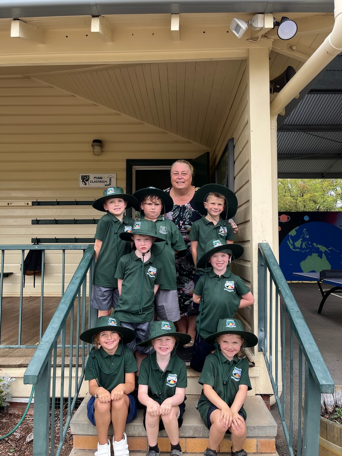 Eight school students standing and sitting on steps with an older woman.