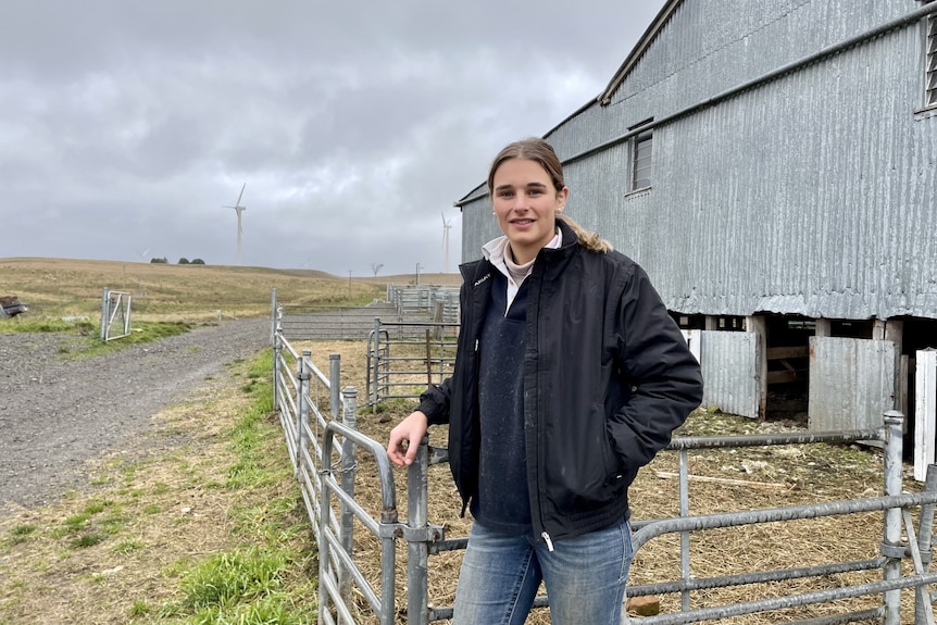 A young woman in a black jacket standing outside a shearing shed