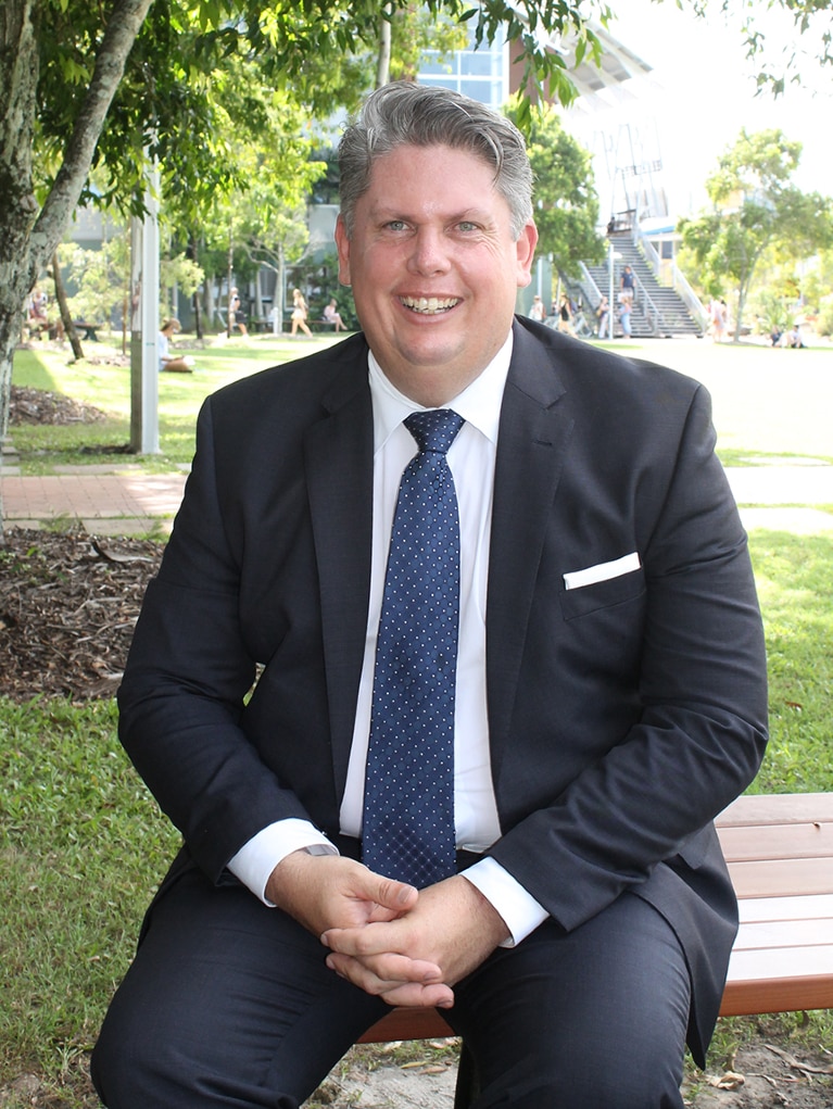 Man in a suit sitting under a tree at a university