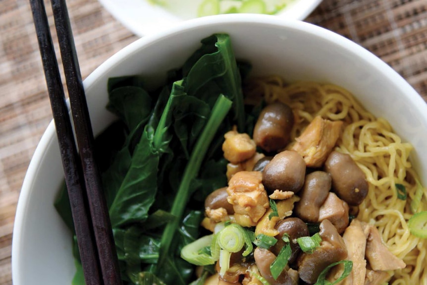 White bowl with mie ayam jamur (egg noodles with chicken and straw mushrooms) and black chopsticks