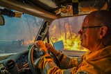 A volunteer firefighter in protective gear drives through a bushfire in Augusta.