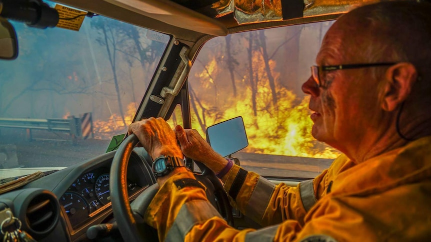 A volunteer firefighter in protective gear drives through a bushfire in Augusta.