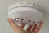 A person's hand screws a smoke alarm into position in a celing.