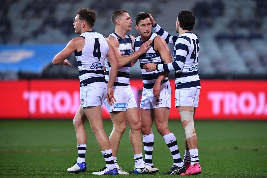A group of Geelong players gather around a teammate who has just scored a goal.