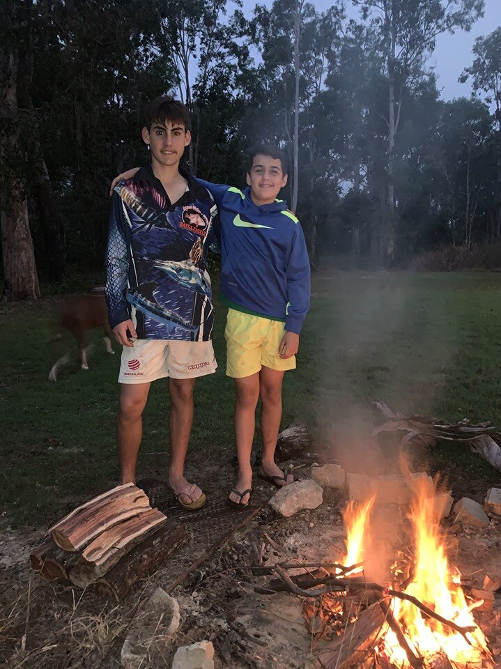 Two boys, arm in arm, enjoy a campfire outside.