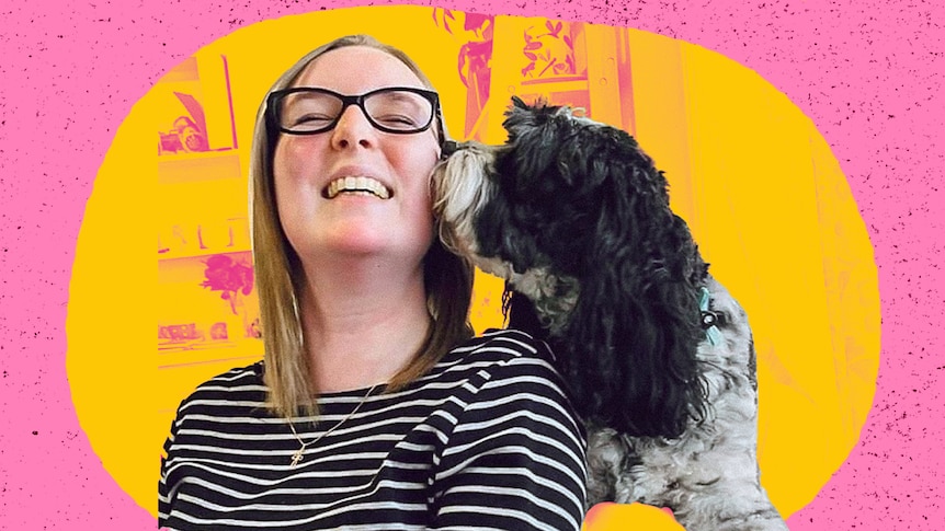 A young woman wearing glasses and a stripey top is being kissed on the cheek by her cute black dog.