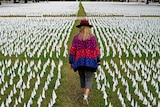 A woman walks through a green field dotted with white flags