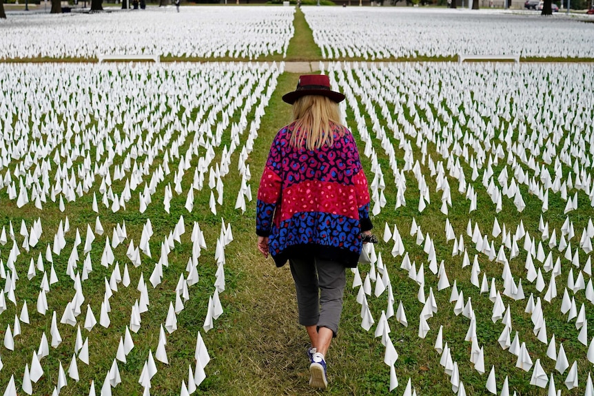 A woman walks through a green field dotted with white flags