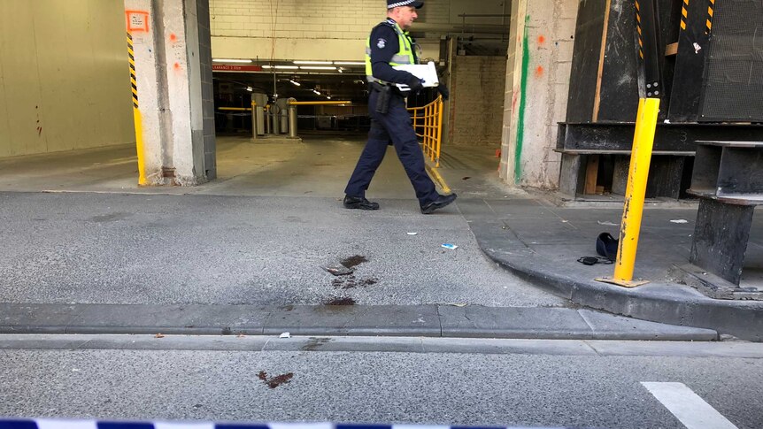 A policeman walks past a trail of blood left on the ground near a car park entrance.