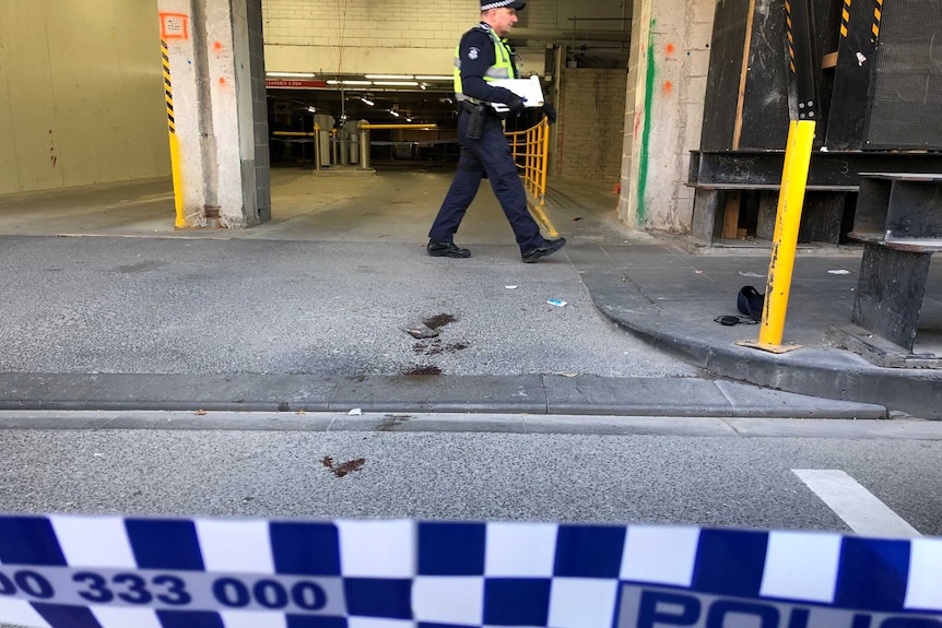 A policeman walks past a trail of blood left on the ground near a car park entrance.