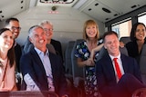 a group of seven people, men and women, smiling at the camera as they sit in a bus
