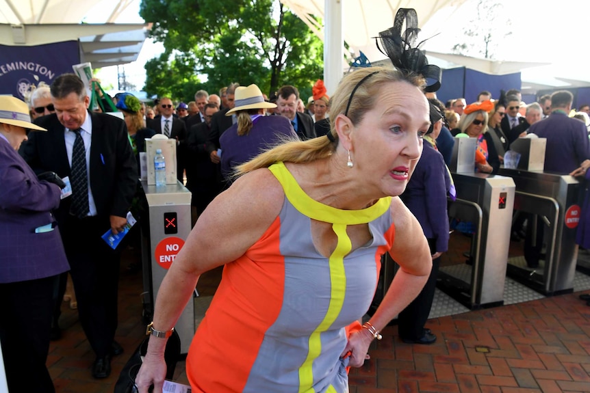A woman in a dress and fascinator bolts through the barriers at Flemington Racecourse.