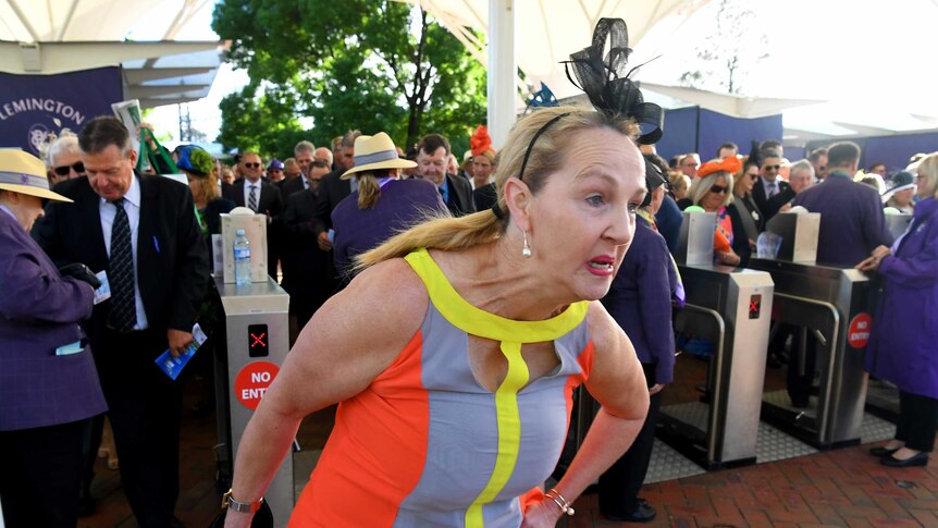 A woman in a dress and fascinator bolts through the barriers at Flemington Racecourse.