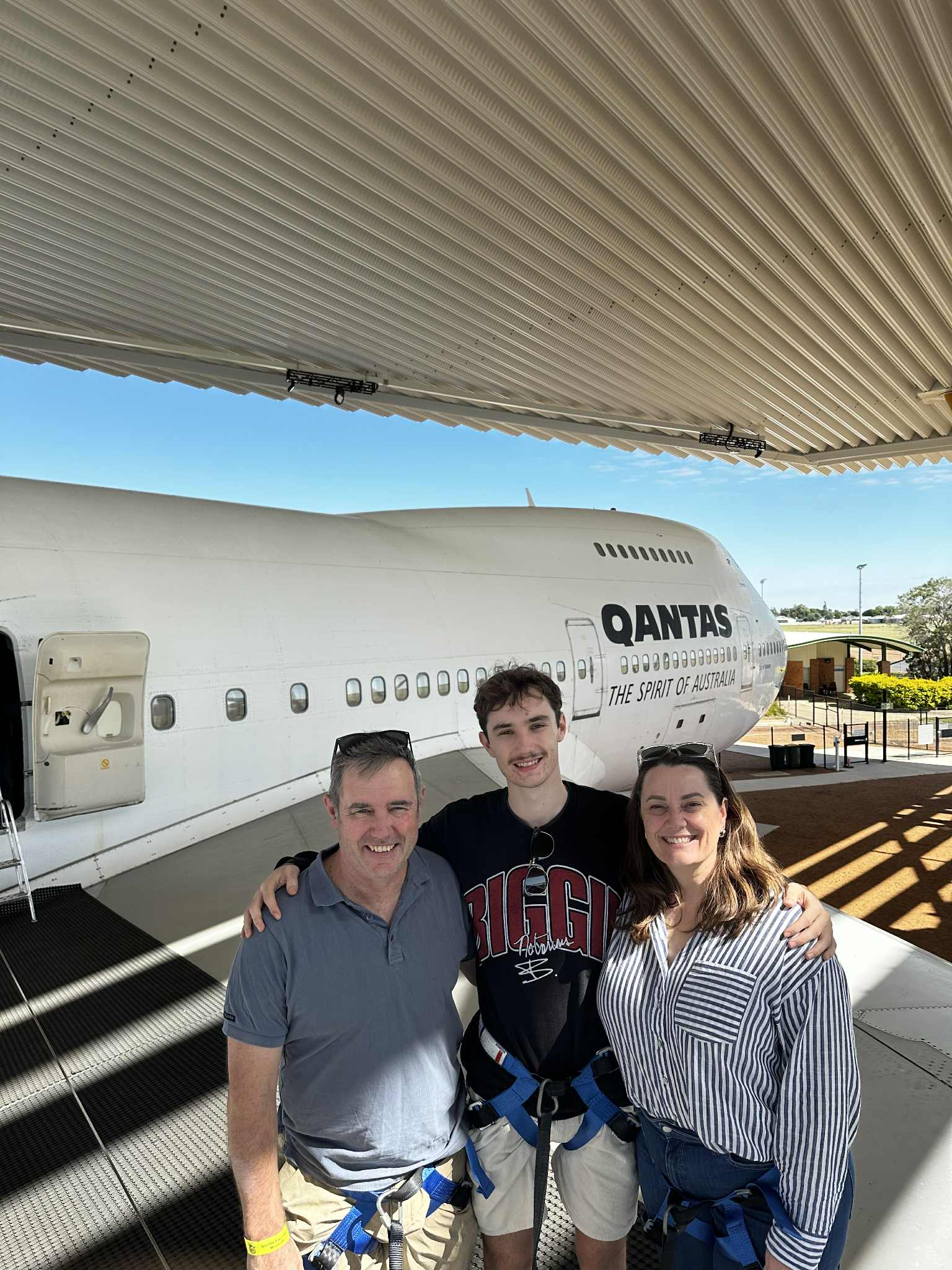 Sam se encuentra frente a un avión de Qantas en Longreah con su esposo y su hijo. 